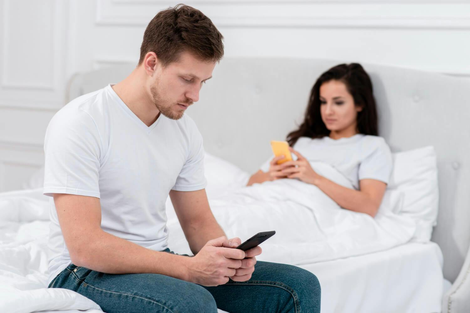 Dos personas en la cama, cada una absorta en sus dispositivos.