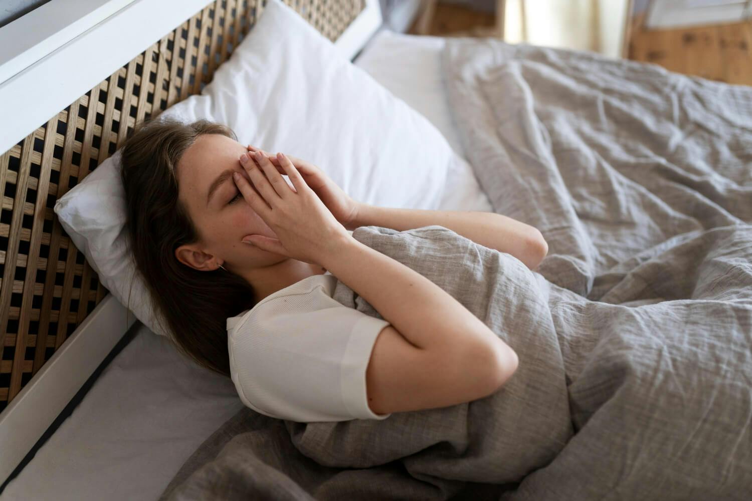 Mujer tumbada en la cama con expresión preocupada, reflejando los síntomas del insomnio y la ansiedad que afectan su capacidad para dormir bien.