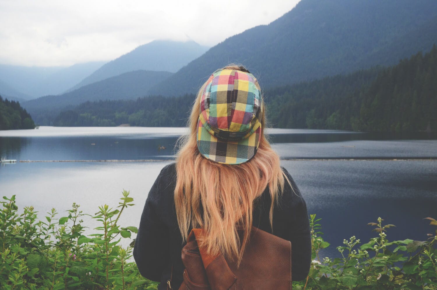 Chica joven con gorra mirando al agua en la naturaleza.