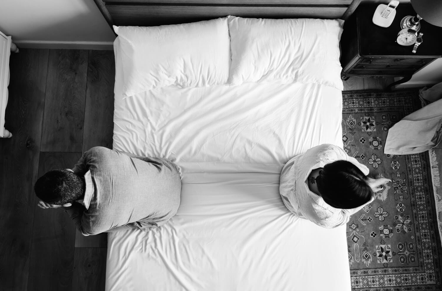 Foto de una pareja interracial sentados espalda con espalda en la cama.