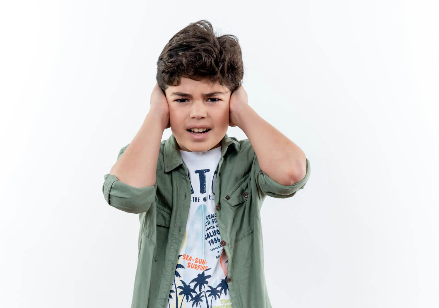 Niño con autismo cubriéndose los oídos ante un ruido fuerte, ejemplificando la sensibilidad sensorial en el autismo infantil.